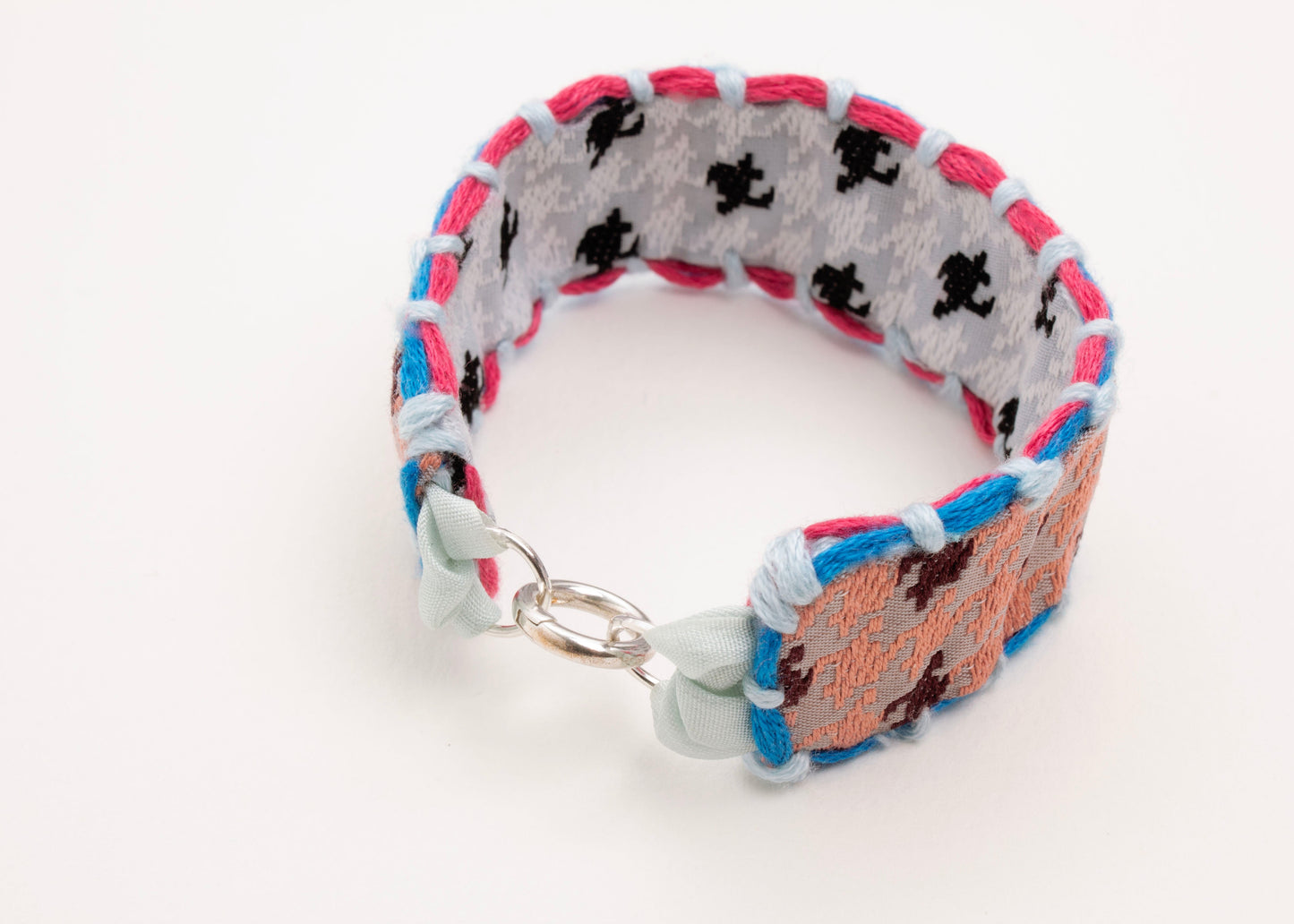 Front view of a reversible cotton woven strap bracelet in houndstooth pattern showing both sides: peach and grey blue with embroidered borders in cyan and fuchsia and Sterling Silver looped endings detail on a white background.