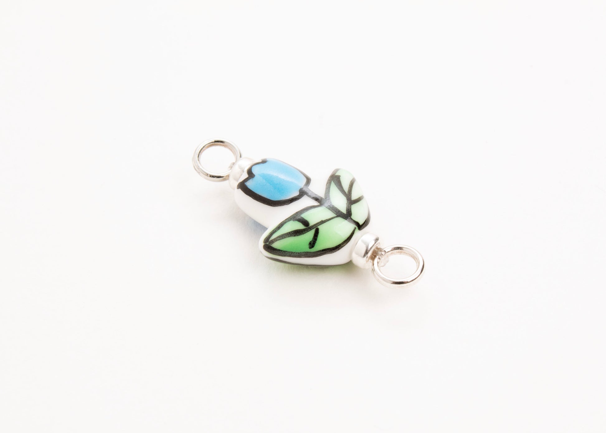 Side diagonal close up of a handprinted light blue_hand painted porcelain_tulip_charm_on a white background