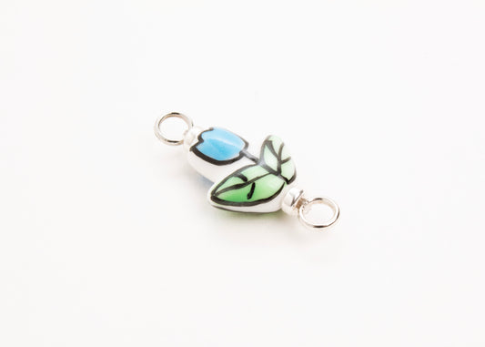 Side diagonal close up of a handprinted light blue_hand painted porcelain_tulip_charm_on a white background