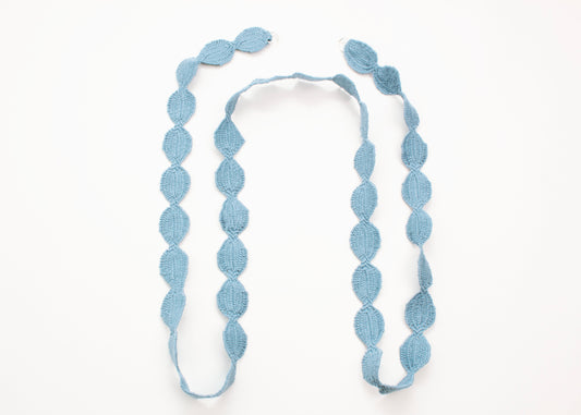 Plan view of a light blue cotton woven ovals necklace in a 'n' shape on a white background. 