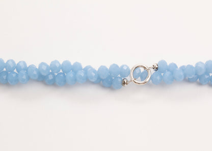 Plan view of a light_blue_glass_beads_strand_closed_twisted_on a white background
