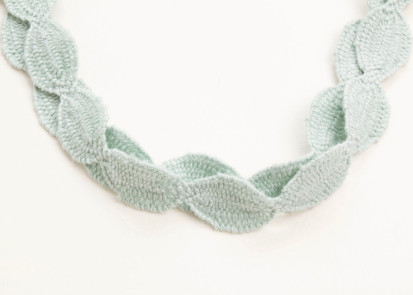 Close up of drop detail of a cotton necklace in light green on a white background