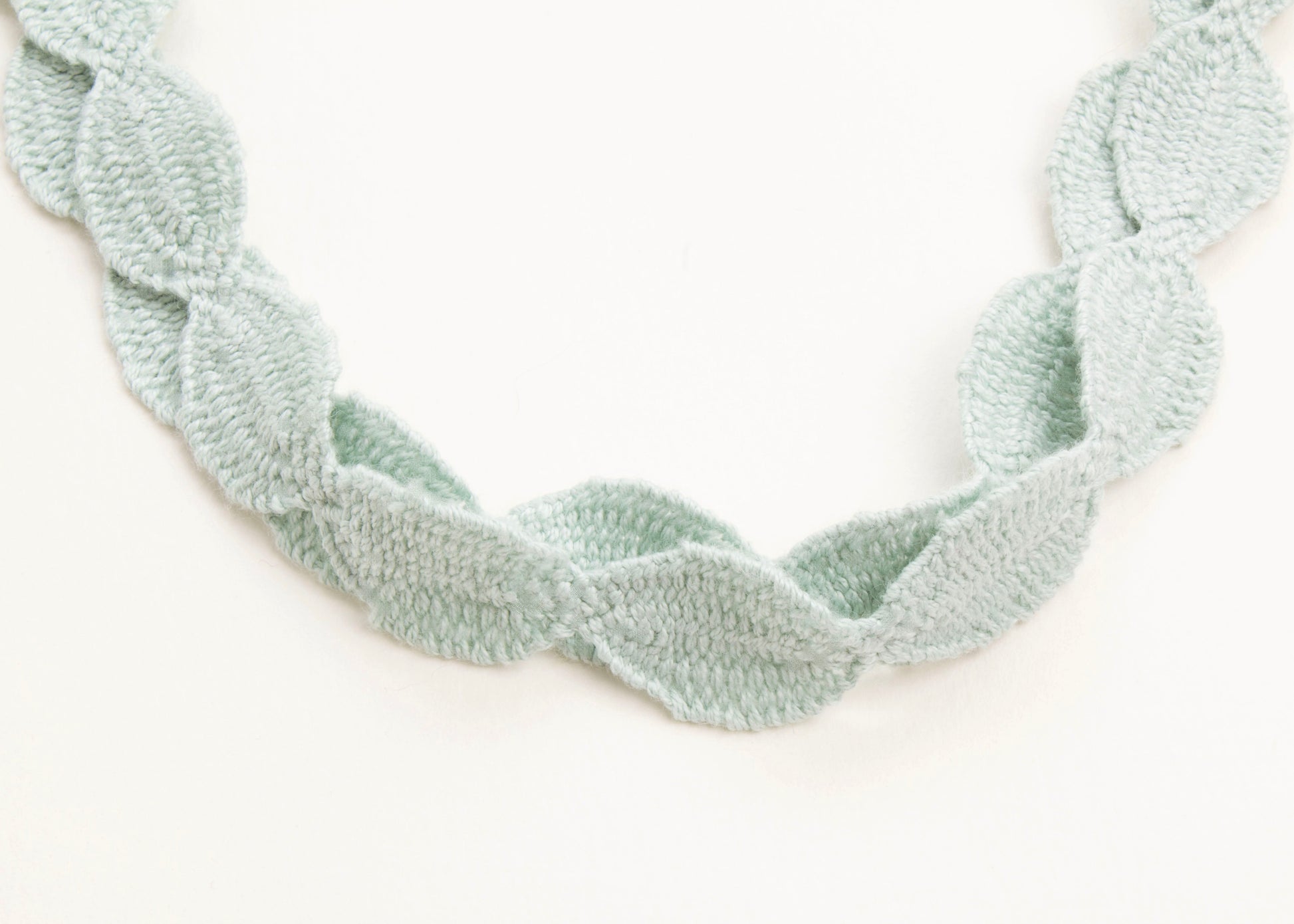 Close up of drop detail of a cotton necklace in light green on a white background