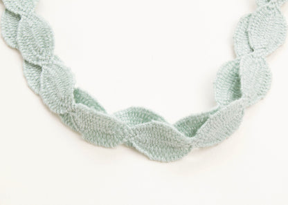 Close up of drop detail of a cotton necklace in light green on a white background