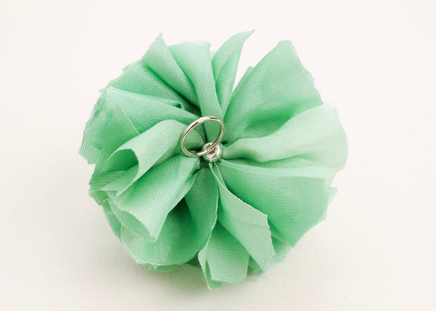 Back view of a light green silk flower charm with sterling silver loop ending on a white background.