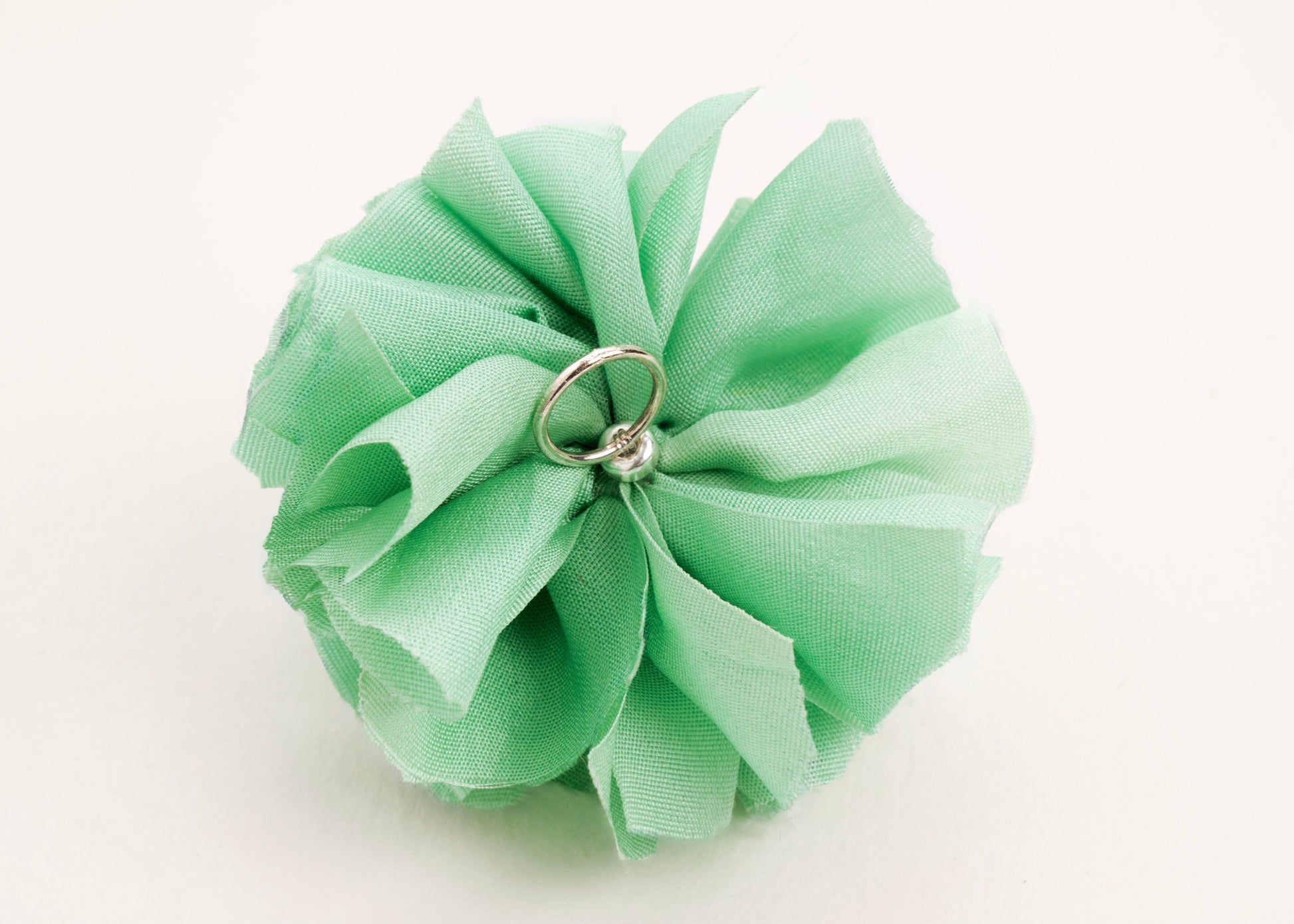 Back view of a light green silk flower charm with sterling silver loop ending on a white background.