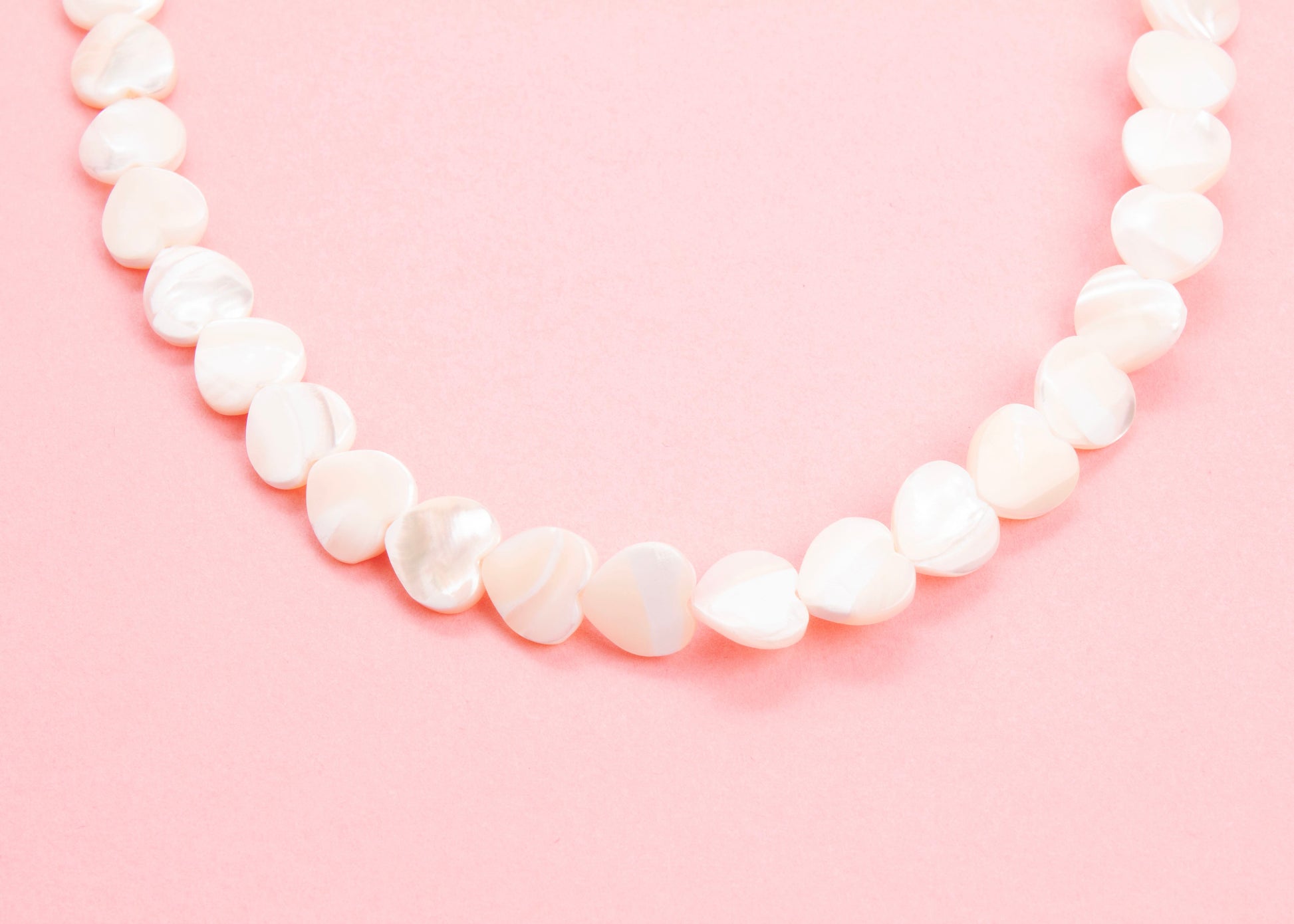 Close up drop detail of a MOP heart beads necklace on a pink background