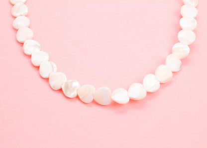 Close up drop detail of a MOP heart beads necklace on a pink background