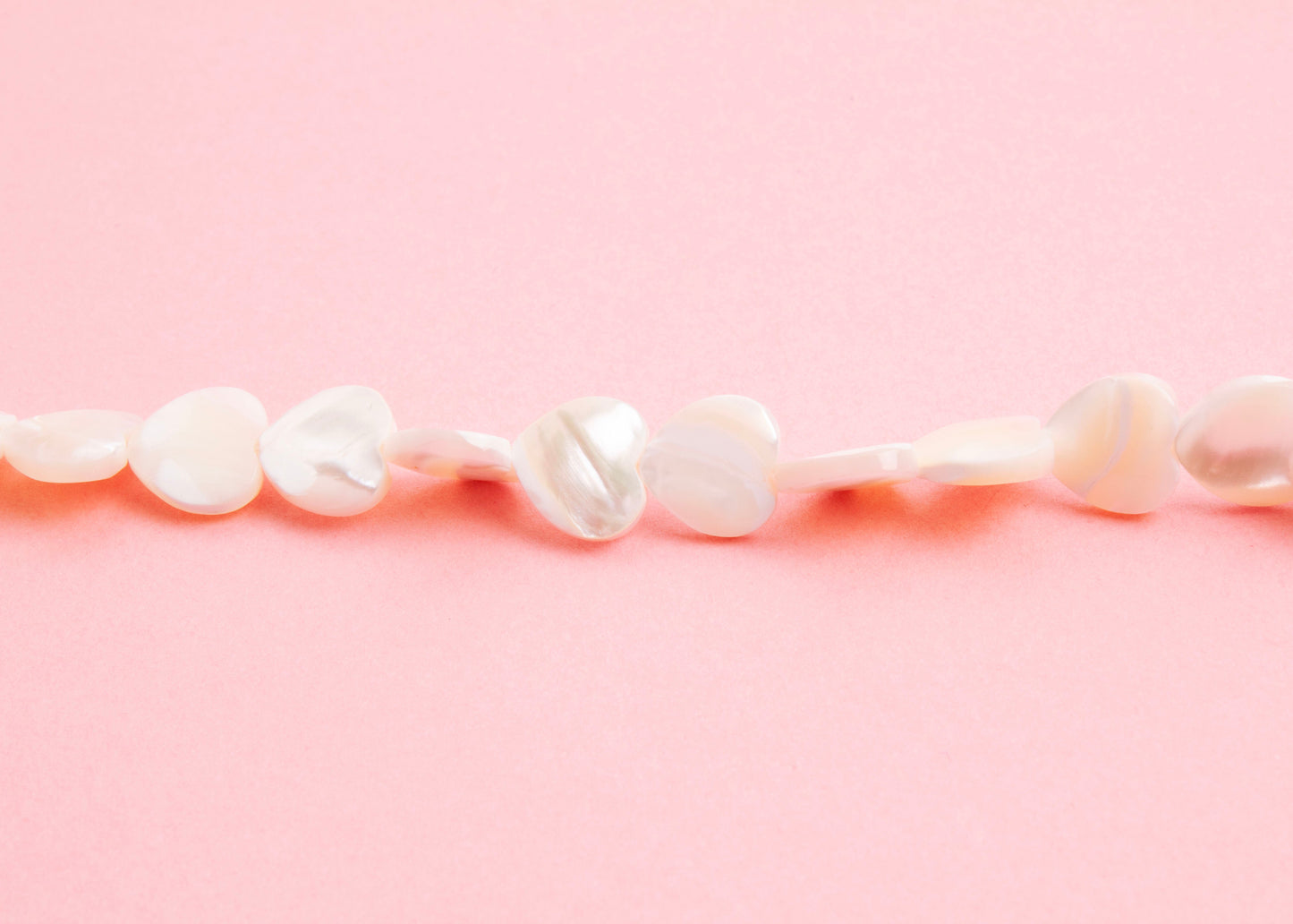 Front view beads detail of a MOP heart beads necklace on a pink background