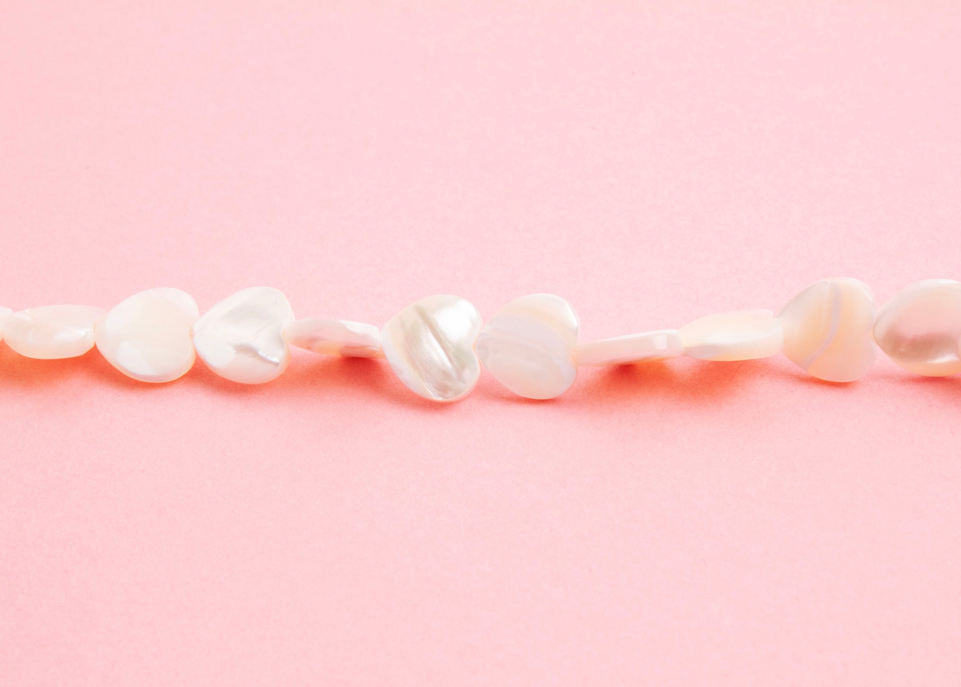 Front view beads detail of a MOP heart beads necklace on a pink background