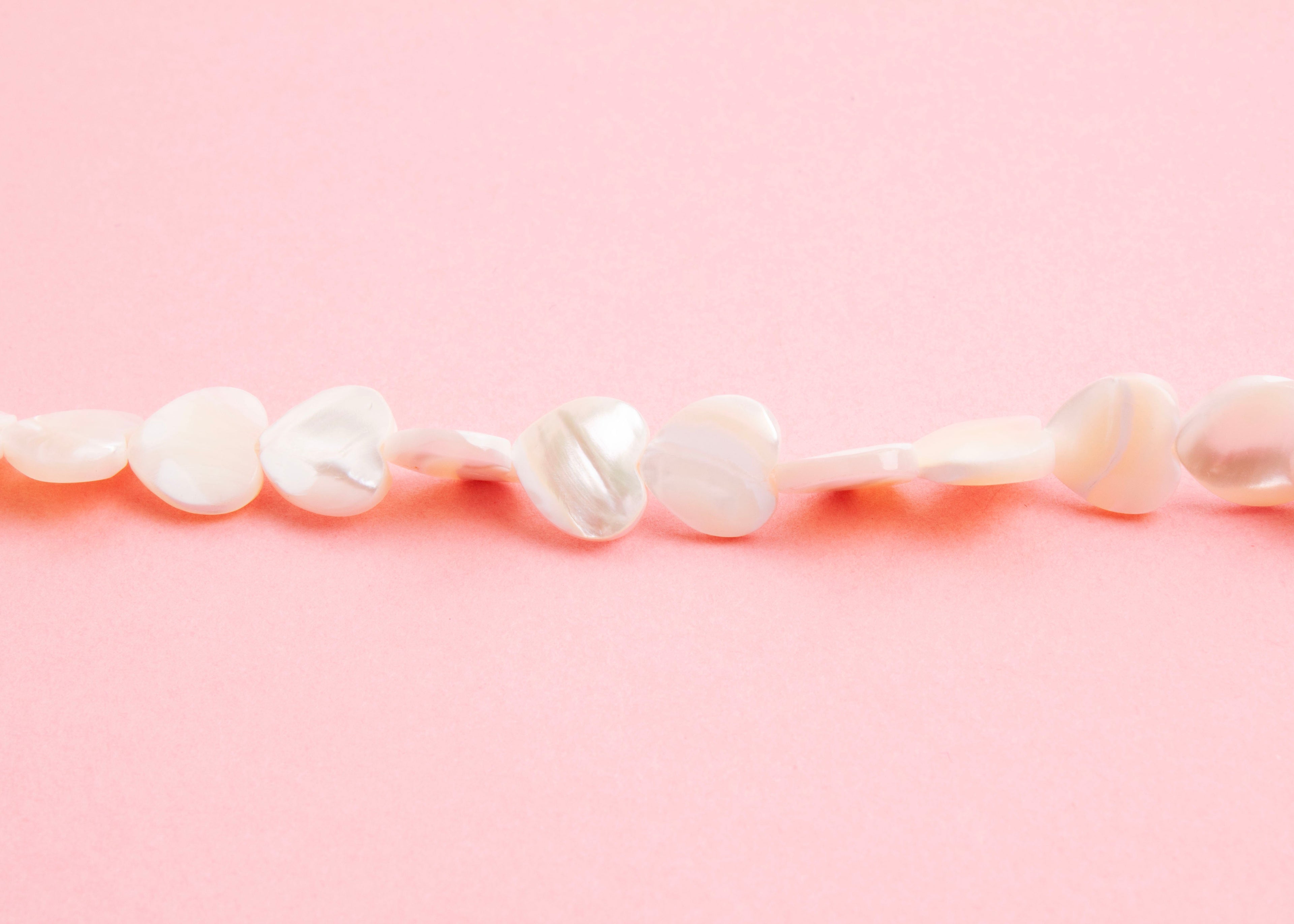 Front view beads detail of a MOP heart beads necklace on a pink background