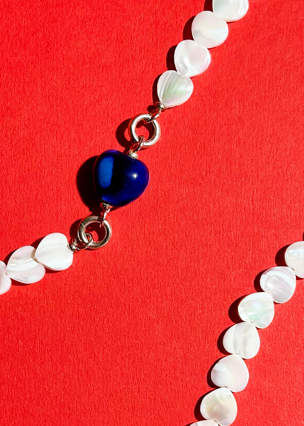 Close up of a chunky blue porcelain charm attached to an MOP heart shaped carved beads necklace with Sterling Silver endings 