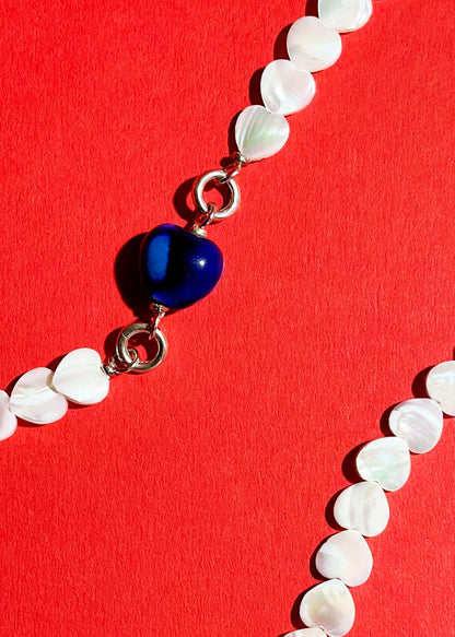 Close up of a chunky blue porcelain charm attached to an MOP heart shaped carved beads necklace with Sterling Silver endings 
