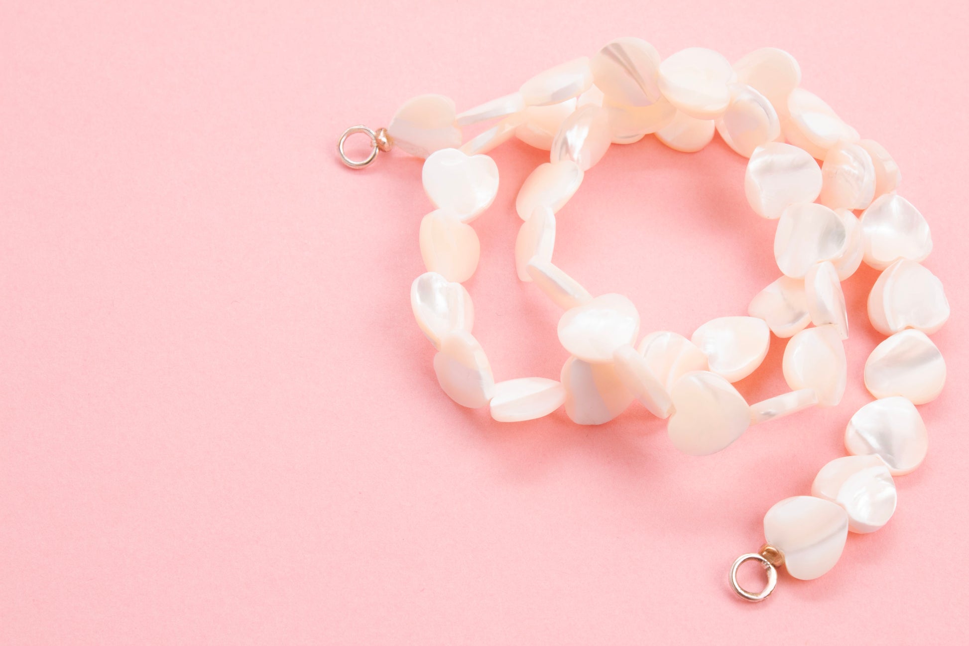 Plan view of a MOP hearts beads necklace with Sterling Silver looped endings on a pink background