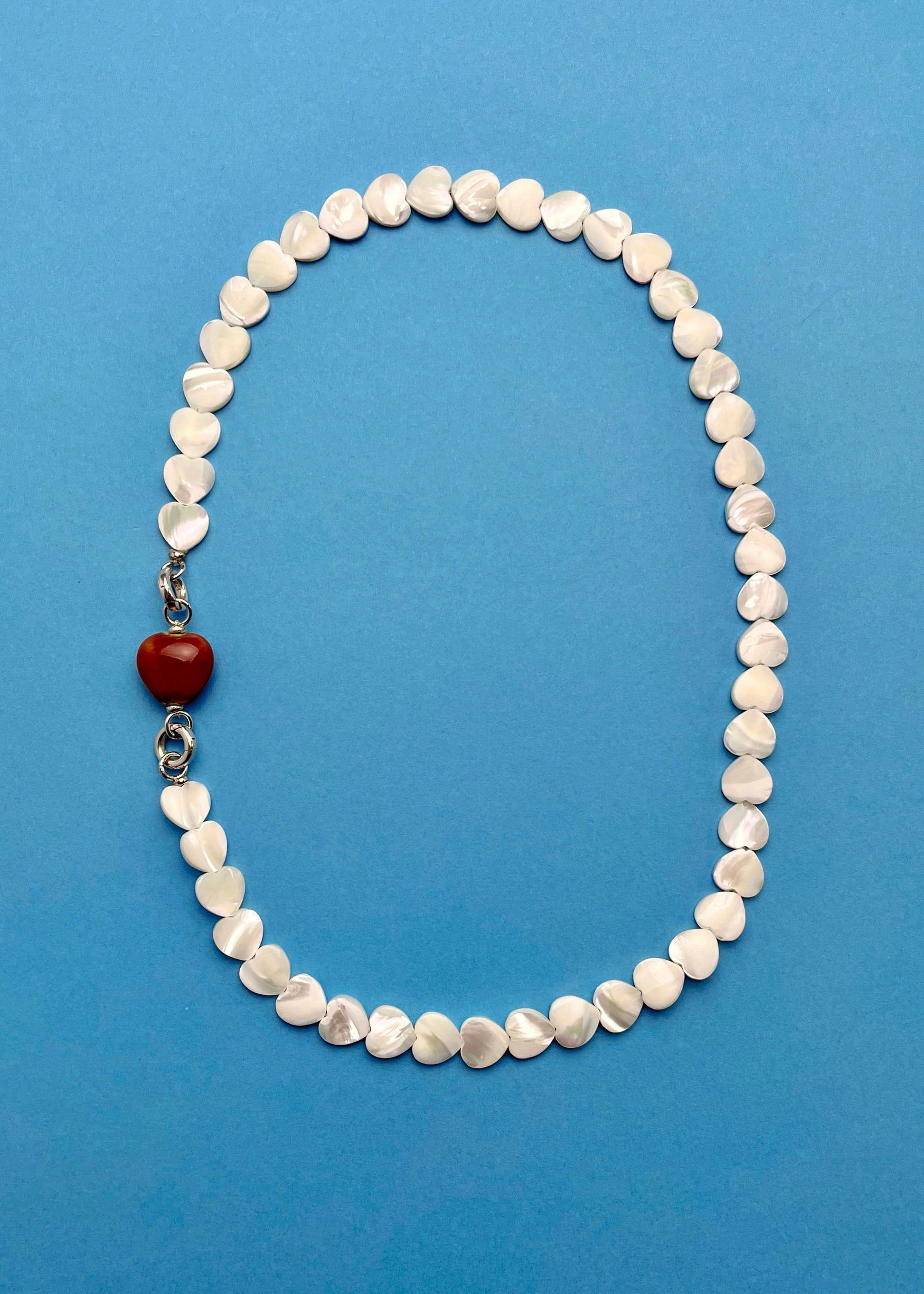 Overhead view of an MOP_necklace_with_red_porcelain_heart_charm attached and Sterling Silver endings _placed on a cerulean background