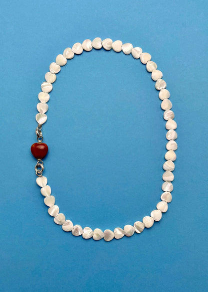 Overhead view of an MOP_necklace_with_red_porcelain_heart_charm attached and Sterling Silver endings _placed on a cerulean background