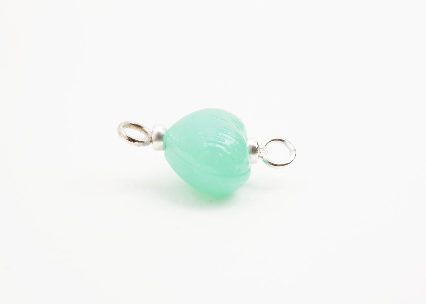 Side horizontal close up of green glass heart charm placed on white background.