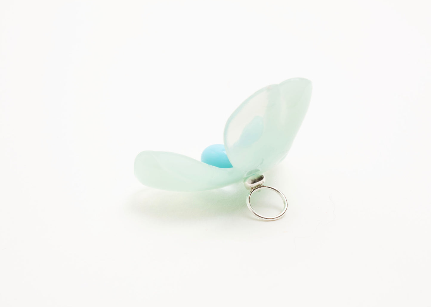 Full back view close up of a mint green resin_flower charm with light blue glass bead detail_and a Sterling Silver looped ending on a white background