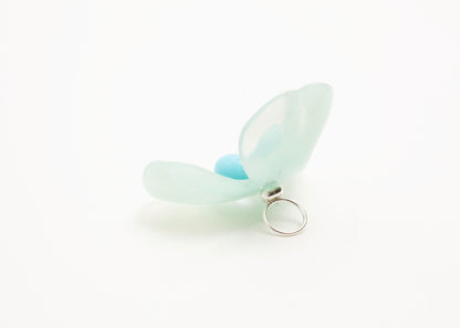 Full back view close up of a mint green resin_flower charm with light blue glass bead detail_and a Sterling Silver looped ending on a white background