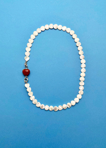 Overhead view of a Mother of Pearl heart beads necklace with a red chunky porcelain heart bead charm and Sterling Silver endings placed on a cyan background
