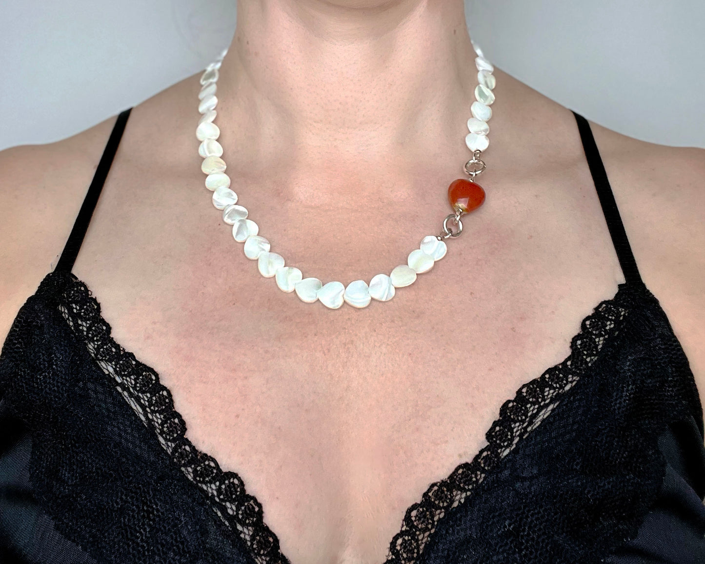 Front view of a woman wearing a Mother of Pearl heart beads necklace with a red chunky porcelain heart bead charm and Sterling Silver endings 