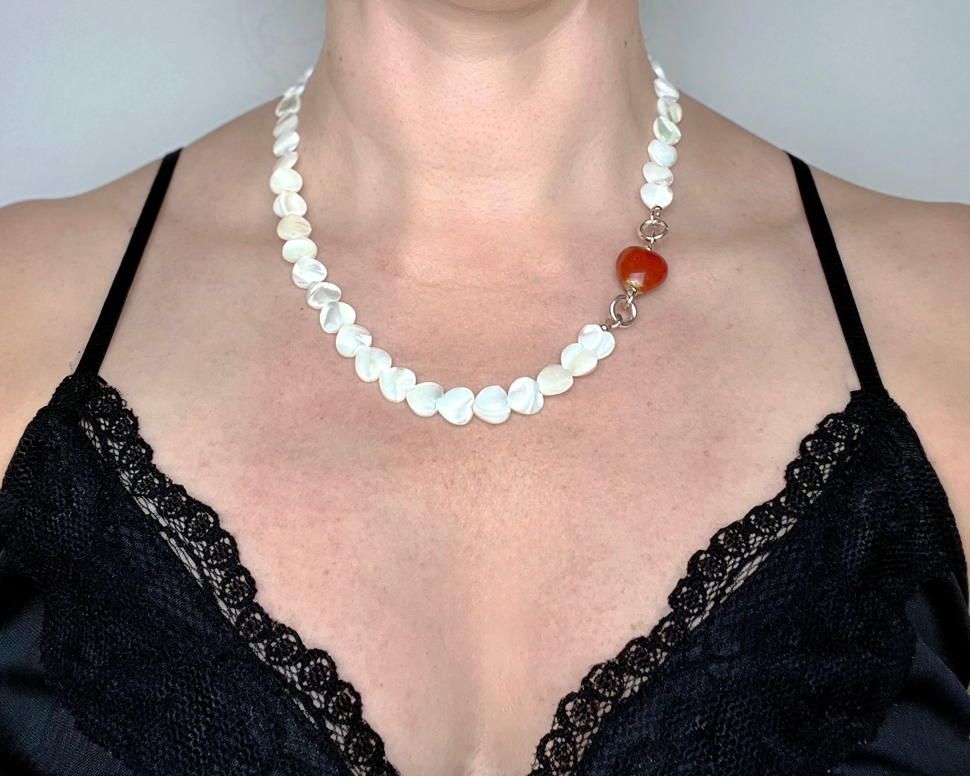 Front view of a woman wearing a Mother of Pearl heart beads necklace with a red chunky porcelain heart bead charm and Sterling Silver endings 