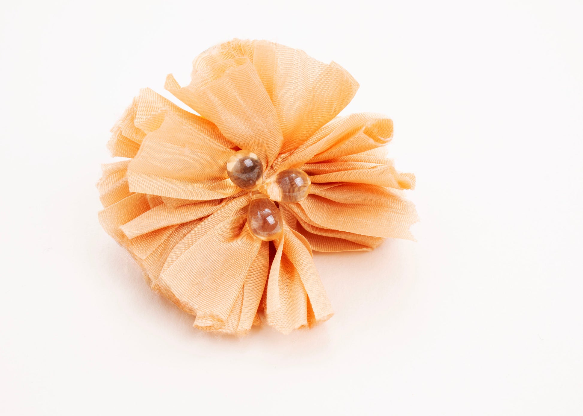 Front view of a peach silk flower charm with glass detail in center on a white background.