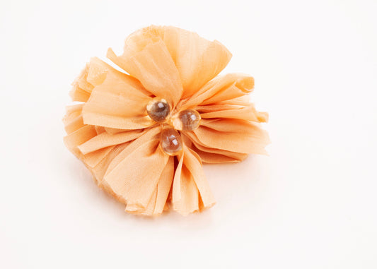 Front view of a peach silk flower charm with glass detail in center on a white background.