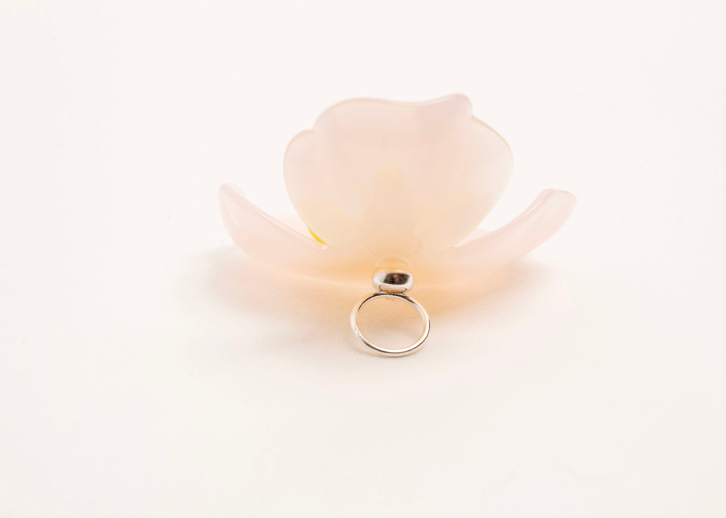 Full back close up of a peach resin_flower charm with yellow glass bead detail_and a Sterling Silver looped ending on a white background