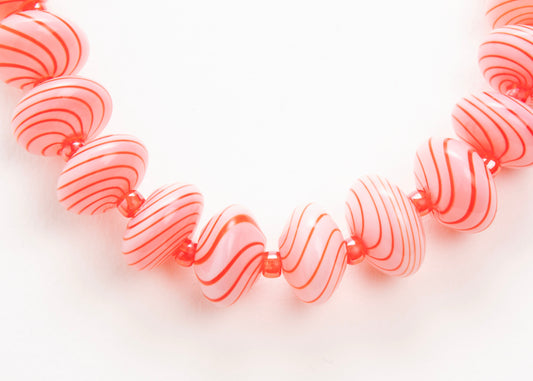Close up of the drop detail of a pink blown glass bead strand with red swirls and red glass separators on a white background