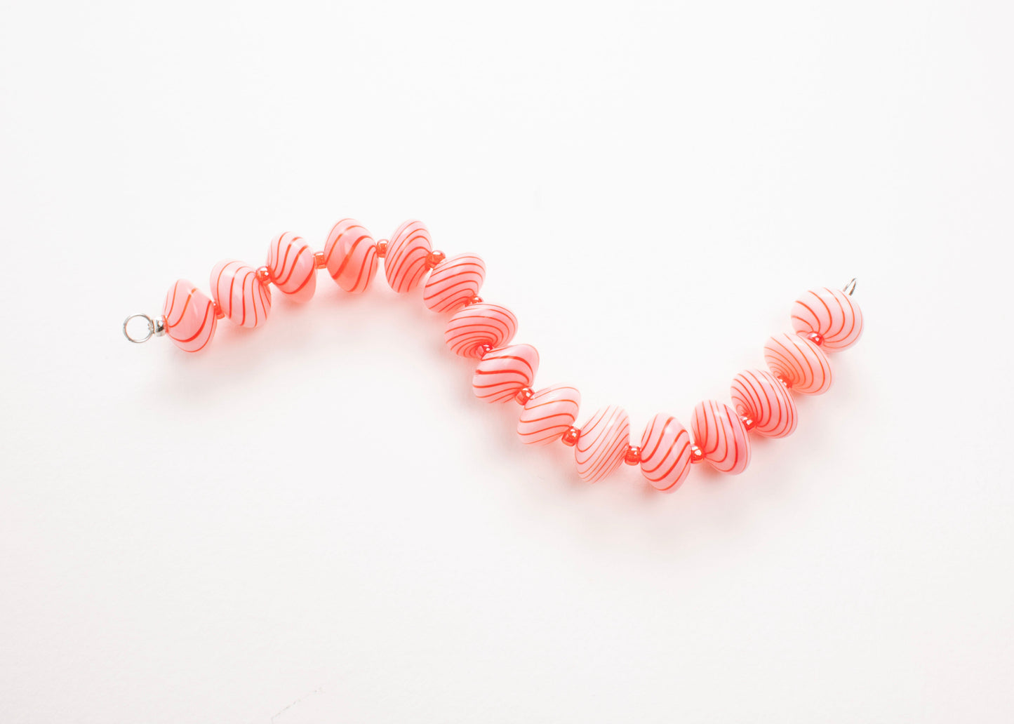 Plan view of a pink blown glass bead strand with red swirls and bright red separators in a zig zag shape on a white background