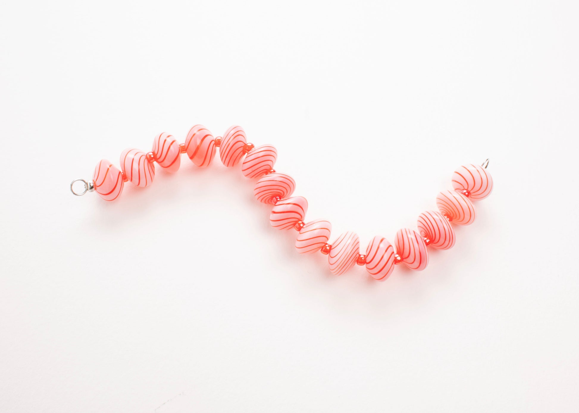 Plan view of a pink blown glass bead strand with red swirls and bright red separators in a zig zag shape on a white background