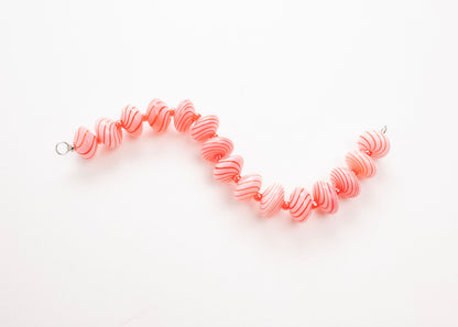 Plan view of a pink blown glass bead strand with red swirls and bright red separators in a zig zag shape on a white background