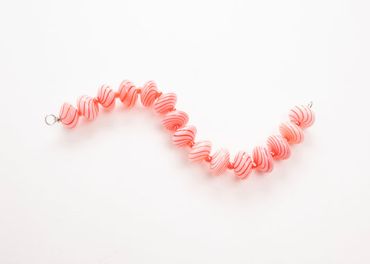 Plan view of a pink blown glass bead strand with red swirls and bright red separators in a zig zag shape on a white background