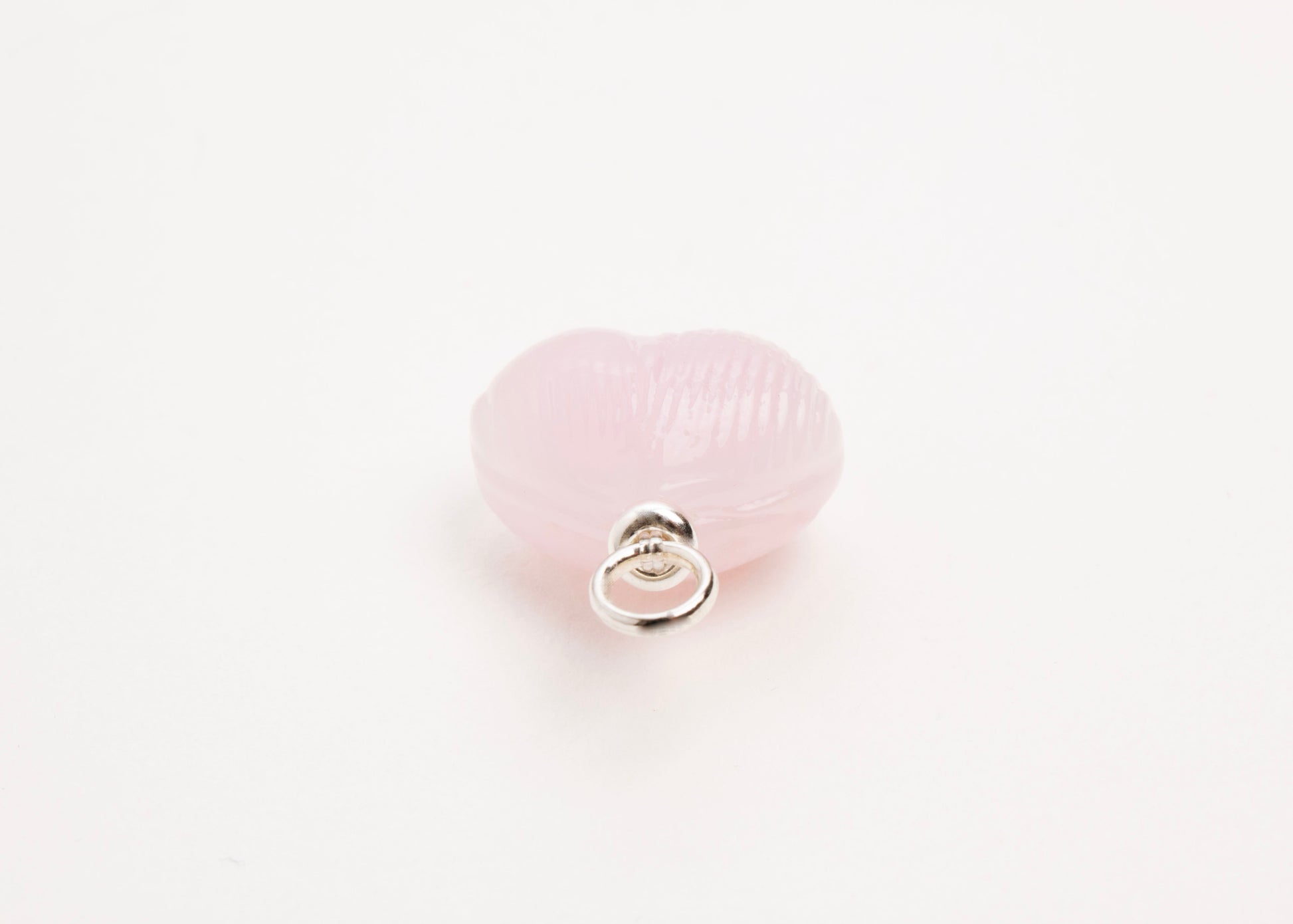 Ending close up of pink glass heart charm placed on white background.