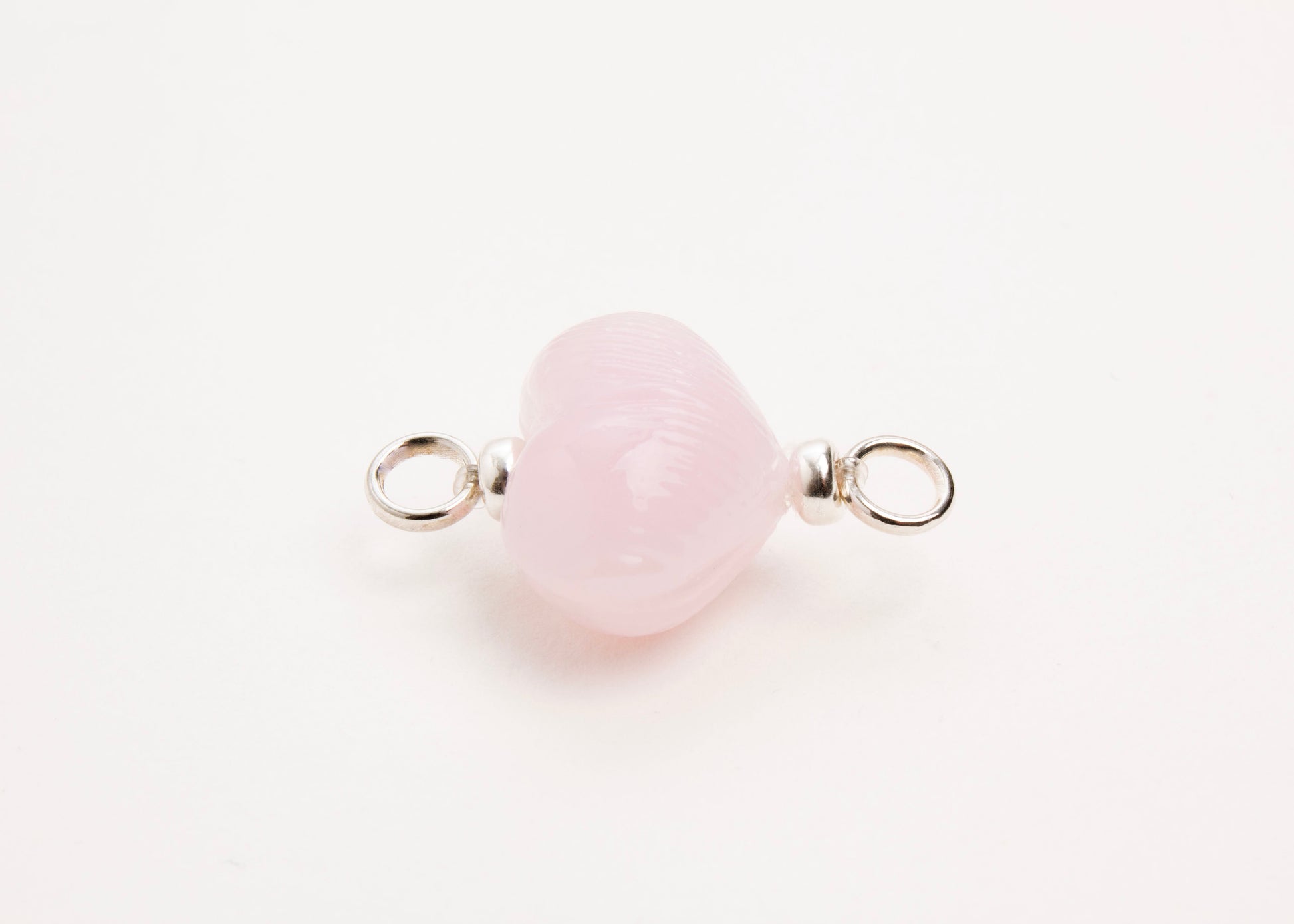 Horizontal close up of pink glass heart charm placed on white background.
