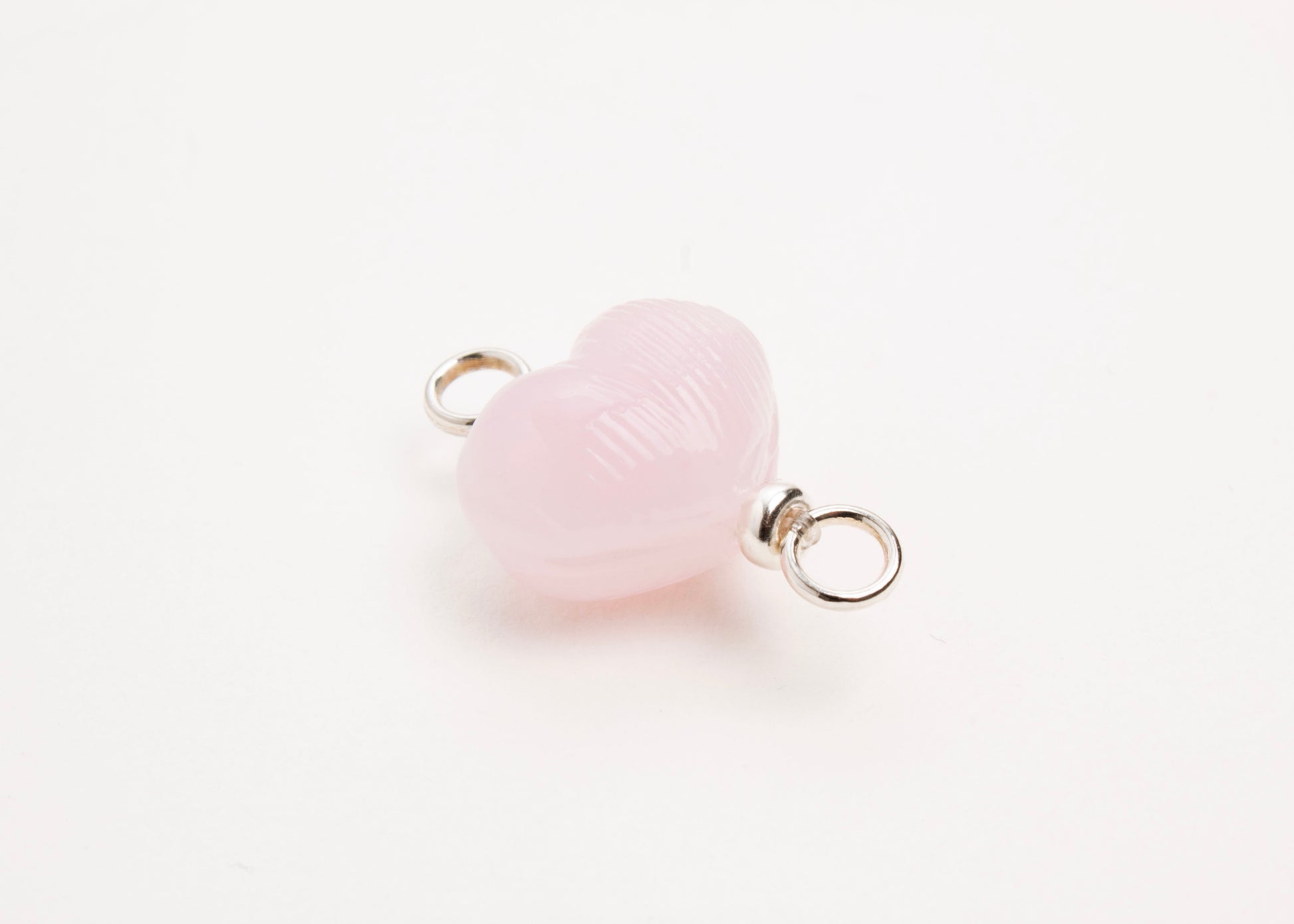 Side diagonal close up of pink glass heart charm placed on white background.