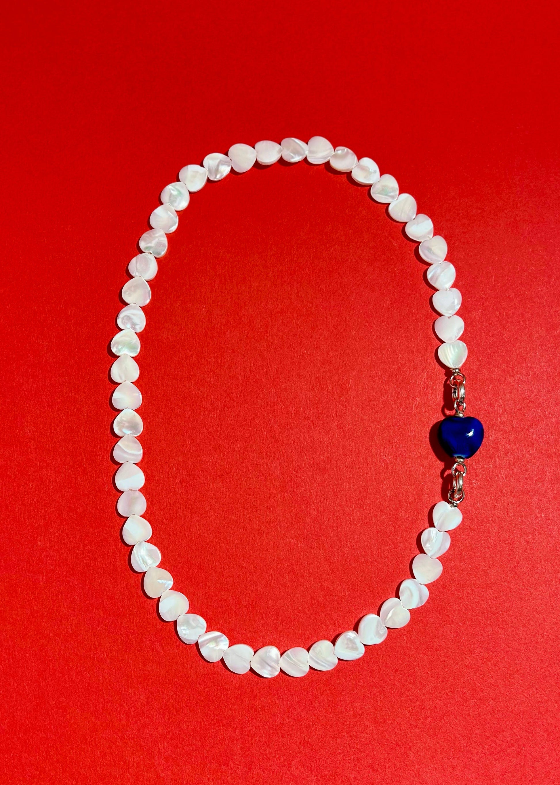 Overhead view of MOP heart shaped carved beads necklace strands with a chunky blue porcelain charm and Sterling Silver endings 