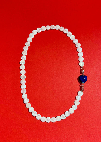 Overhead view of MOP heart shaped carved beads necklace strands with a chunky blue porcelain charm and Sterling Silver endings 