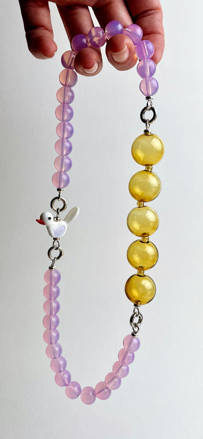 Front view of a hand holding a ready to wear necklace made with deep pink Opalite chainlets, mellow yellow chunky glass bead drop and lamp work glass bird charm with Sterling Silver endings on a white background