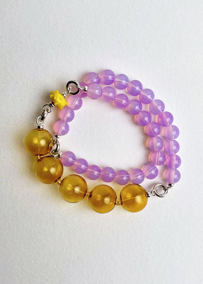Overhead view of a ready to wear deep pink Opalite chainlets, mellow yellow chunky glass bead drop and a bumpy glass charm with Sterling Silver endings on a white background
