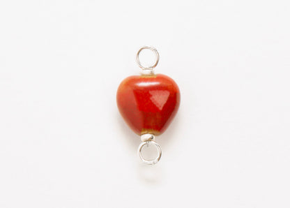 Front close up of a red glazed porcelain heart-shaped charm  with sterling silver looped endings on a white background. 