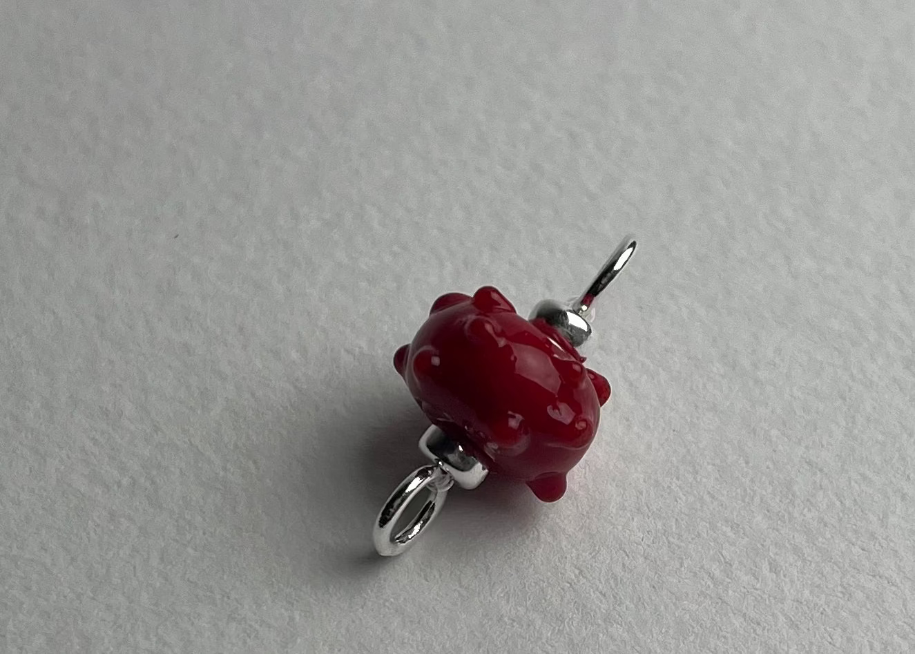 Close up of a red urchin shaped bumpy lampwork charm with sterling silver ends on a white background
