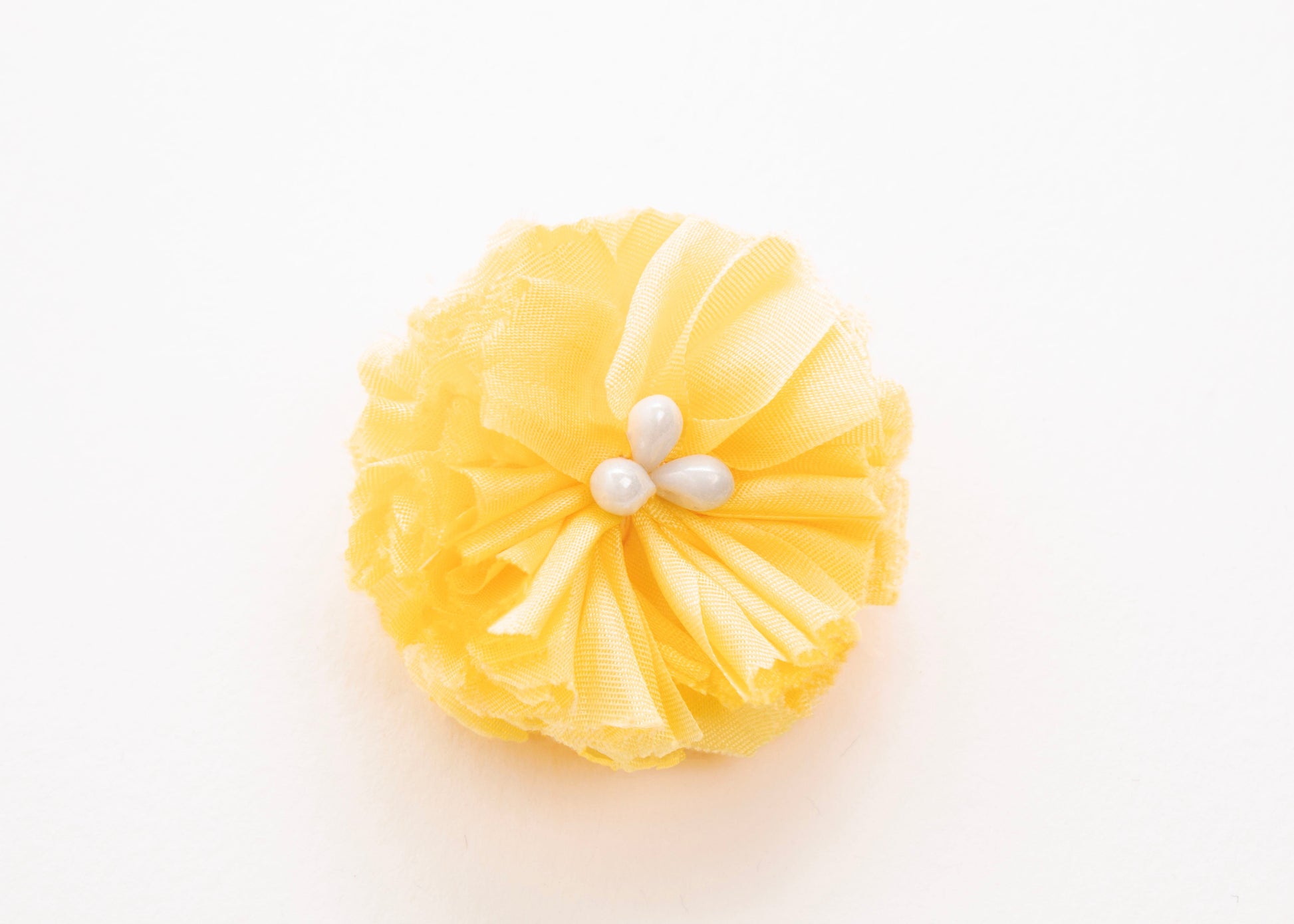 Bright yellow flower connector and charm with pearled white glass bead trio in the centre on a white background.