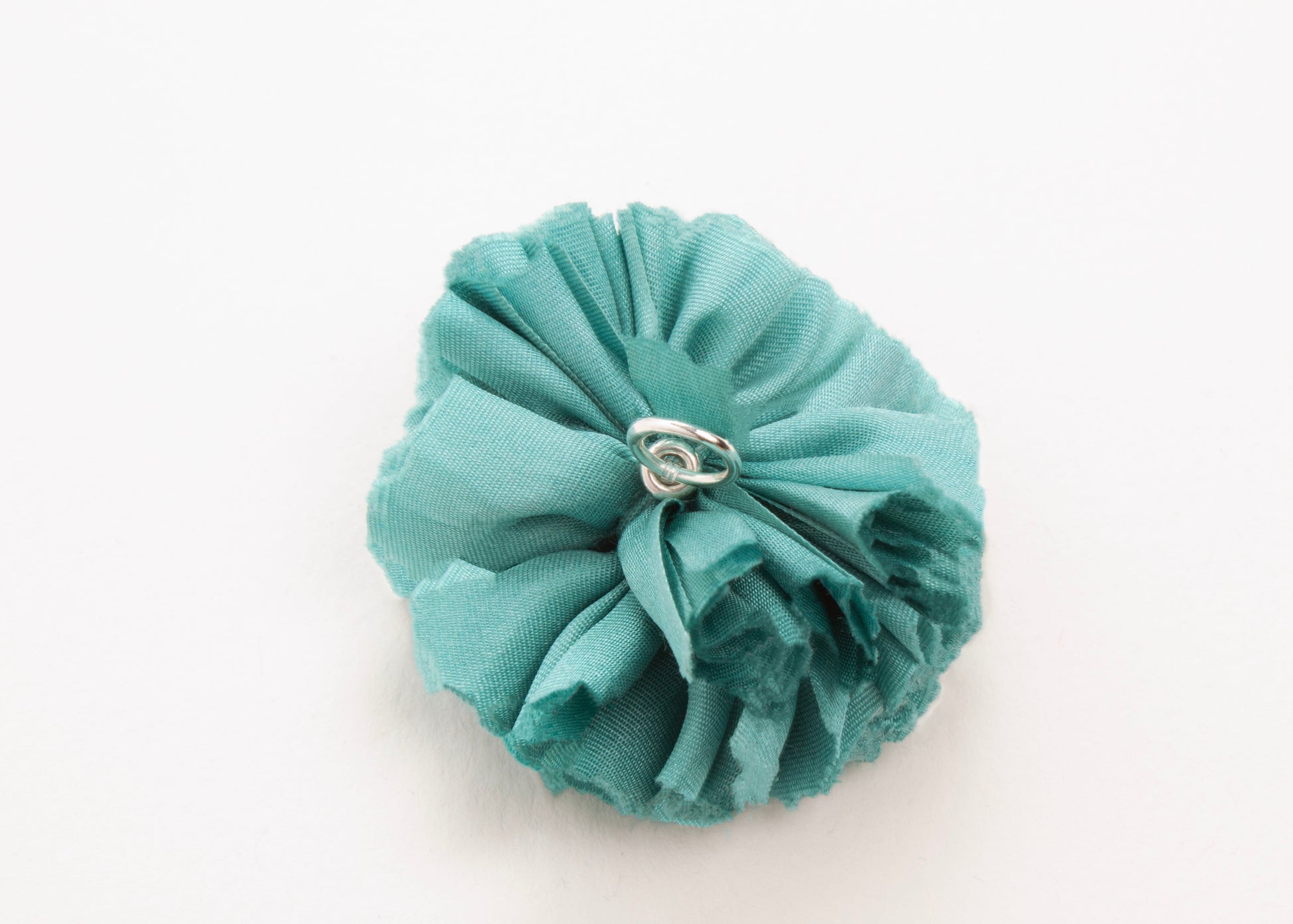 Teal flower connector and charm with sterling silver looped ending on a white background
