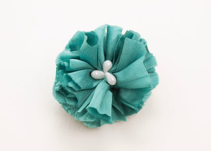 Teal flower connector and charm with pearled white glass beads in the centre on a white background.