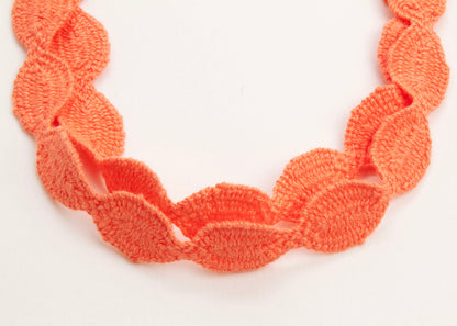 Close up of the drop detail of an orange red cotton woven ovals necklace on a white background