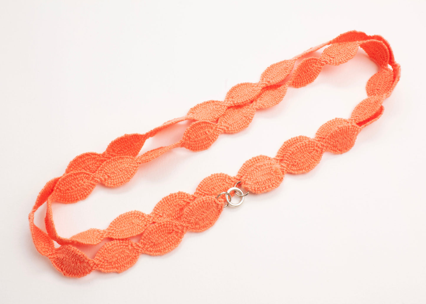 Plan view of a orange red cotton woven ovals necklace with Sterling Silver looped ends on a white background