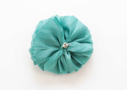 Back view of a teal silk flower charm with sterling silver loop end on a white background.