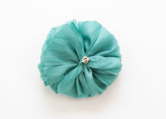 Back view of a teal silk flower charm with sterling silver loop end on a white background.